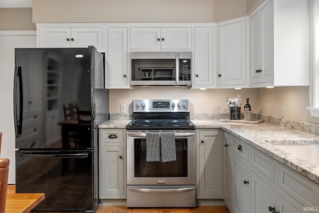 kitchen with appliances with stainless steel finishes, white cabinetry, and light stone counters