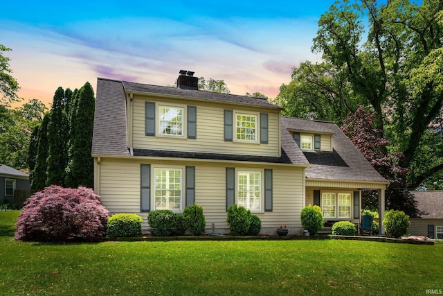 view of front of property featuring a yard, a chimney, and a shingled roof