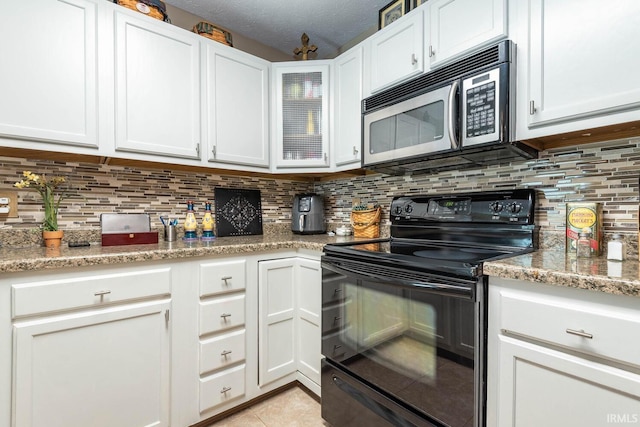 682 E Heather Dr, Bloomington, IN 47401 - kitchen with black electric range, stainless steel microwave, light tile patterned floors, and white cabinets