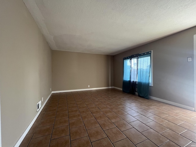 tiled spare room featuring a textured ceiling and baseboards