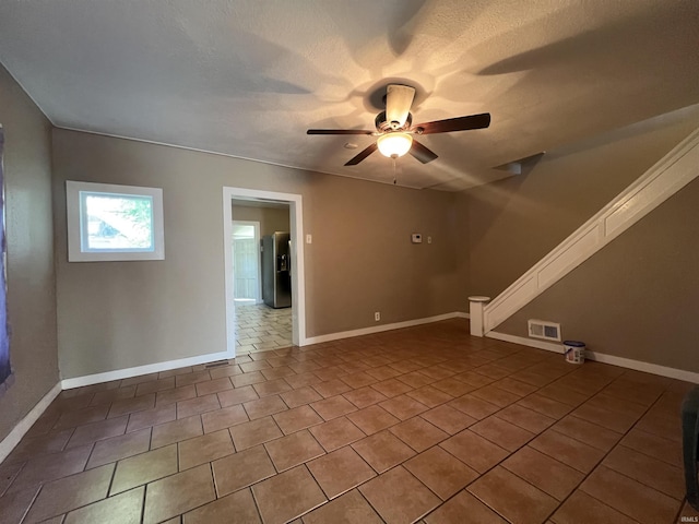 tiled spare room with ceiling fan, baseboards, and a textured ceiling