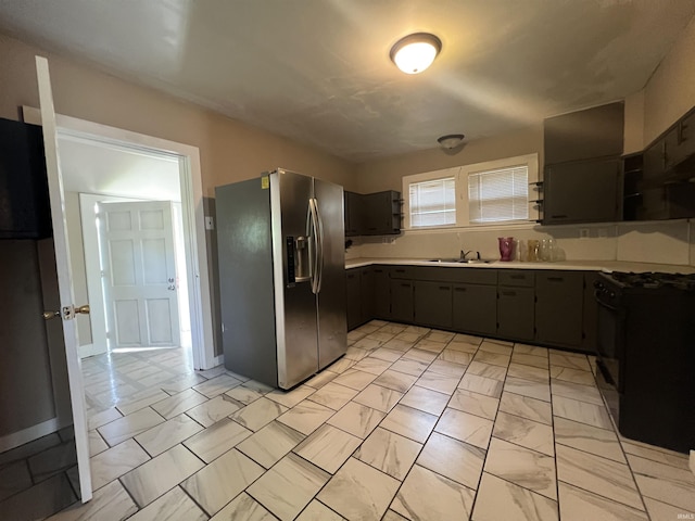 kitchen with stainless steel refrigerator with ice dispenser, black range with gas cooktop, a sink, light countertops, and light marble finish flooring