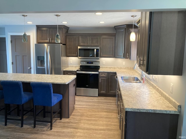 kitchen featuring appliances with stainless steel finishes, a sink, light countertops, light wood-style flooring, and a kitchen breakfast bar
