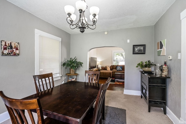 dining room with arched walkways, a chandelier, a textured ceiling, baseboards, and light carpet