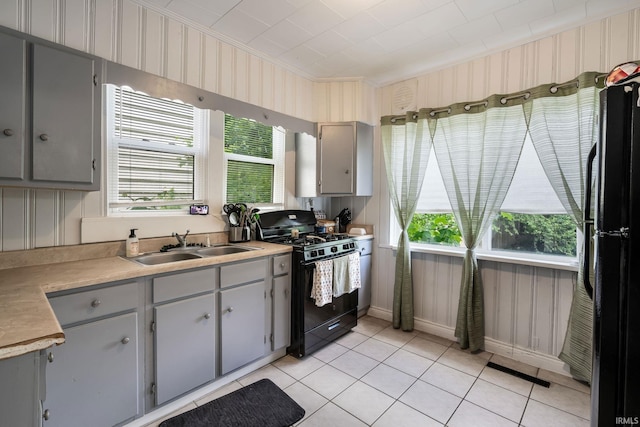 kitchen featuring black gas stove, gray cabinetry, a sink, light tile patterned floors, and light countertops