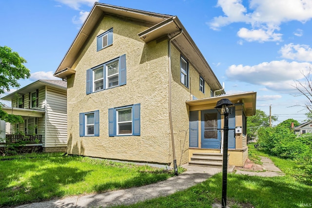 view of side of property with stucco siding, a lawn, and entry steps