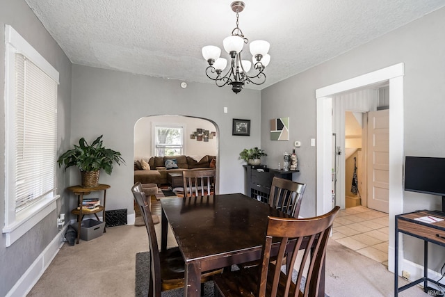 dining room featuring arched walkways, a textured ceiling, a chandelier, and light colored carpet