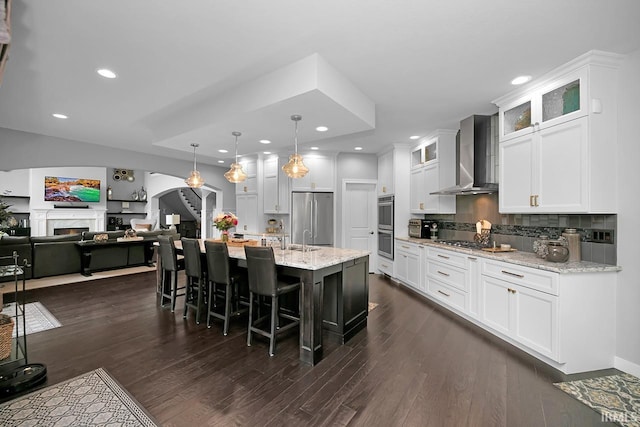 19861 County Road 16, Bristol, IN 46507 - kitchen featuring wall chimney exhaust hood, stainless steel appliances, a lit fireplace, dark wood finished floors, and a kitchen breakfast bar