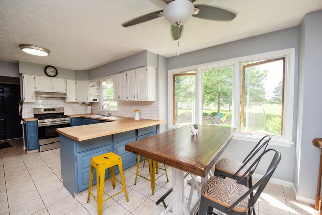 kitchen featuring blue cabinets, wooden counters, gas stove, a sink, and white cabinetry