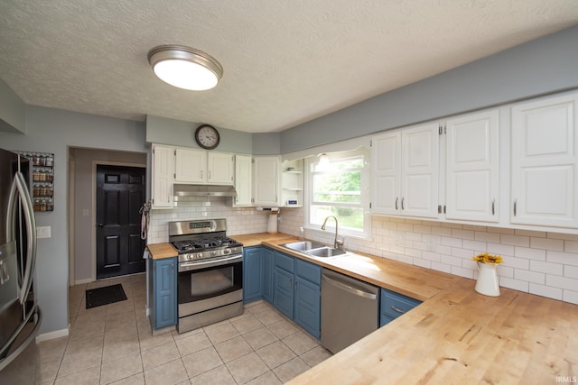 kitchen featuring wood counters, stainless steel appliances, blue cabinetry, a sink, and under cabinet range hood