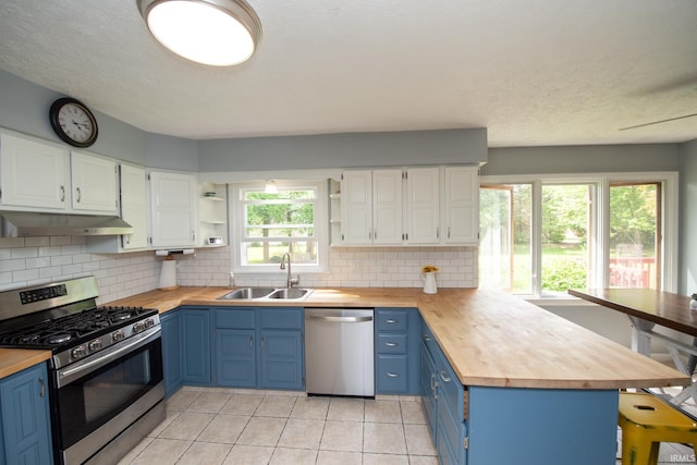 kitchen featuring stainless steel appliances, a sink, butcher block counters, blue cabinetry, and a textured ceiling