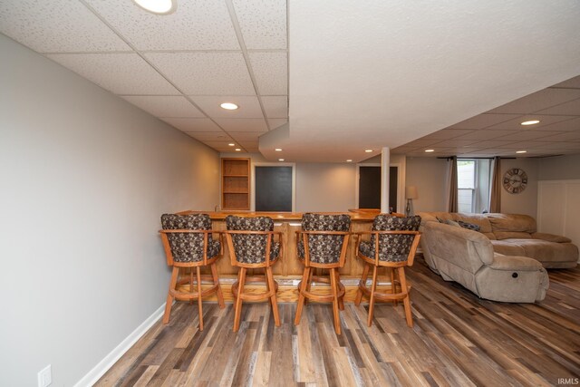 dining area featuring wood finished floors, a bar, baseboards, a paneled ceiling, and recessed lighting