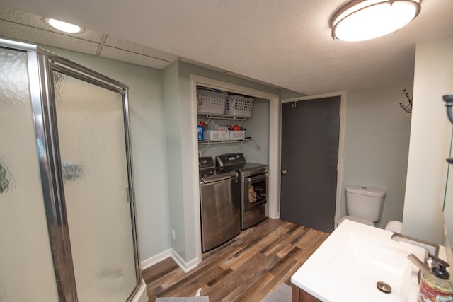 full bathroom featuring washing machine and clothes dryer, wood finished floors, a shower stall, vanity, and toilet
