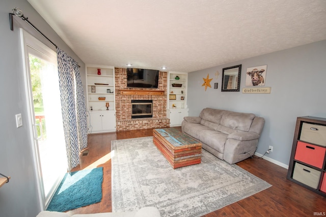 living room featuring a brick fireplace, dark wood-style flooring, baseboards, built in shelves, and a textured ceiling