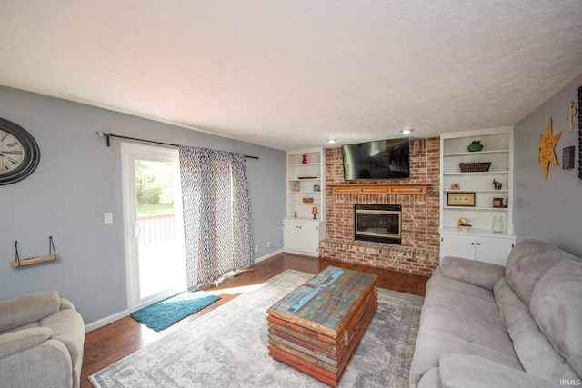 living room featuring wood finished floors, baseboards, a brick fireplace, built in features, and a textured ceiling