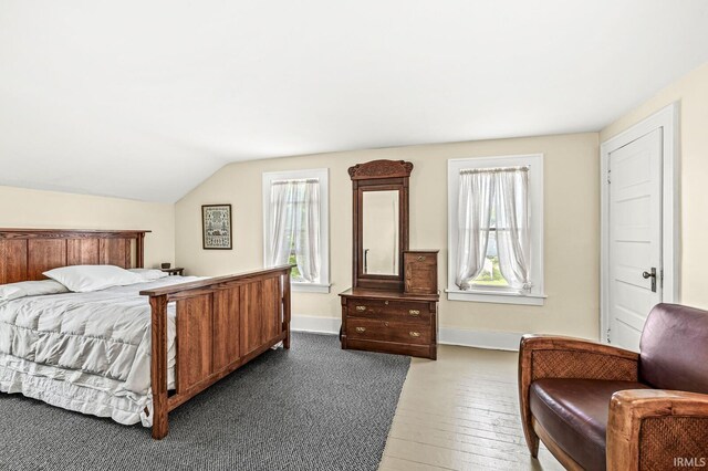 bedroom featuring lofted ceiling, baseboards, and hardwood / wood-style flooring