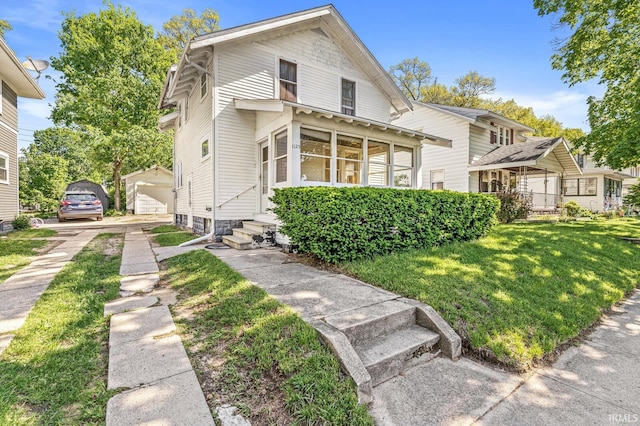 view of front of home with entry steps, a front lawn, a sunroom, a detached garage, and an outdoor structure