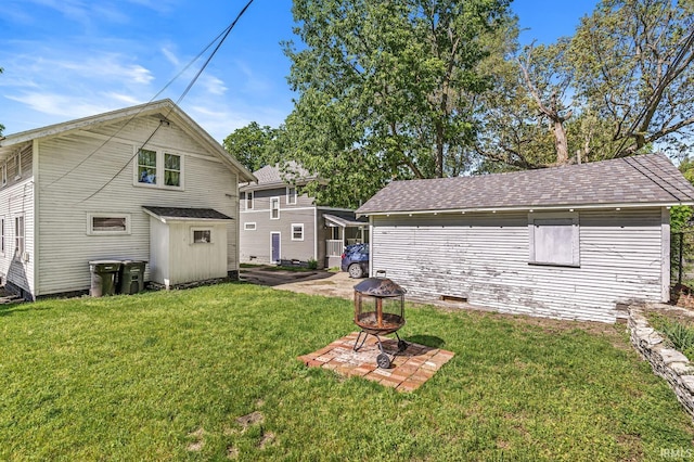 back of house with a fire pit, a lawn, roof with shingles, and an outdoor structure