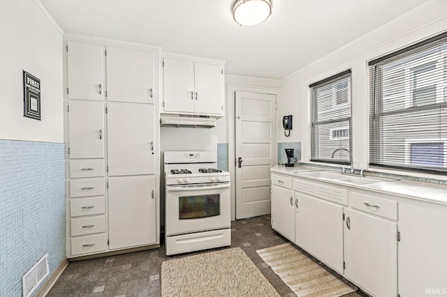 kitchen featuring white gas range oven, a sink, under cabinet range hood, and plenty of natural light