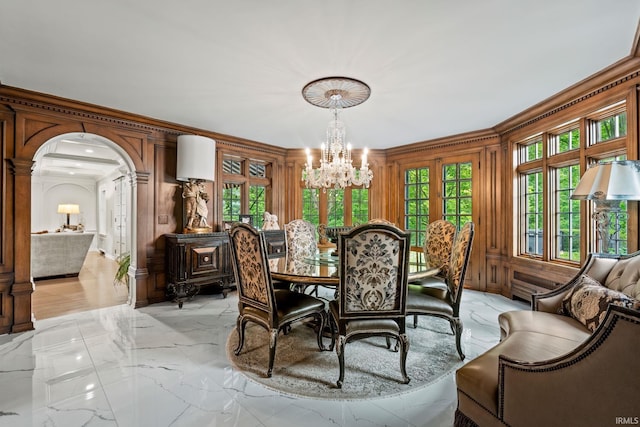 dining room featuring a chandelier, light marble finish floors, crown molding, and arched walkways