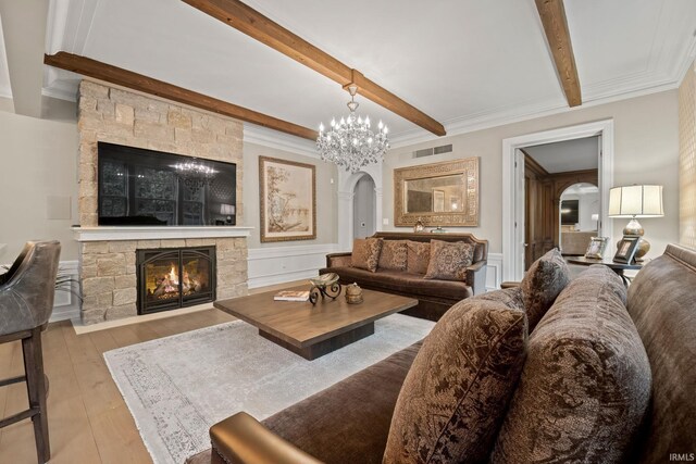 living area featuring arched walkways, beam ceiling, a stone fireplace, hardwood / wood-style flooring, and a chandelier