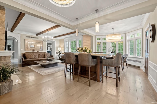 dining room with a chandelier, ornamental molding, beam ceiling, light wood-type flooring, and a decorative wall