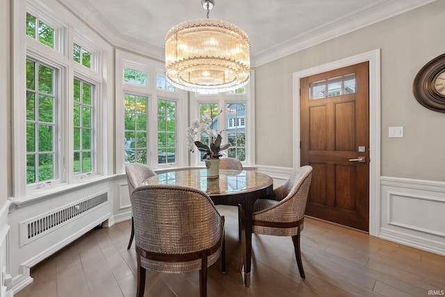 dining space with a chandelier, crown molding, wood finished floors, wainscoting, and a decorative wall