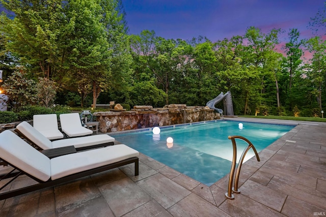pool at dusk featuring a water slide, a patio, an outdoor pool, and an outdoor hangout area