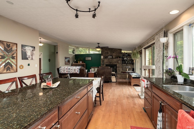 kitchen featuring ceiling fan, brown cabinets, a fireplace, light wood-style floors, and a sink