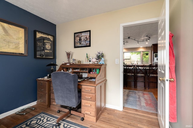 office area with light wood-style floors, baseboards, and a textured ceiling