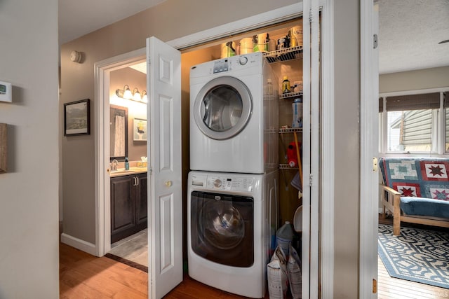washroom with stacked washer / drying machine, light wood-style flooring, and baseboards