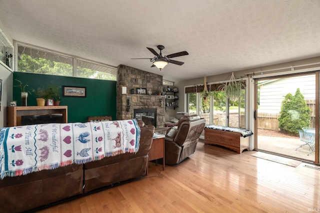 living area featuring lofted ceiling, wood finished floors, ceiling fan, a textured ceiling, and a stone fireplace