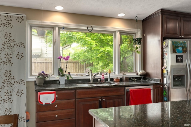 kitchen with stainless steel fridge with ice dispenser, a sink, dishwasher, and dark stone countertops