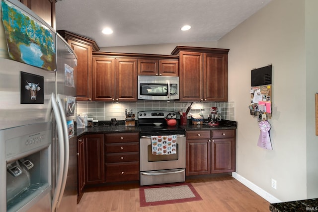 kitchen with appliances with stainless steel finishes, lofted ceiling, light wood finished floors, backsplash, and dark stone countertops