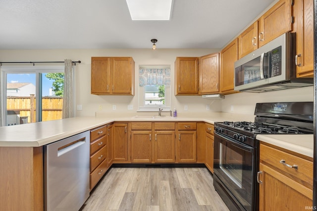 kitchen featuring appliances with stainless steel finishes, light wood finished floors, a peninsula, a sink, and light countertops