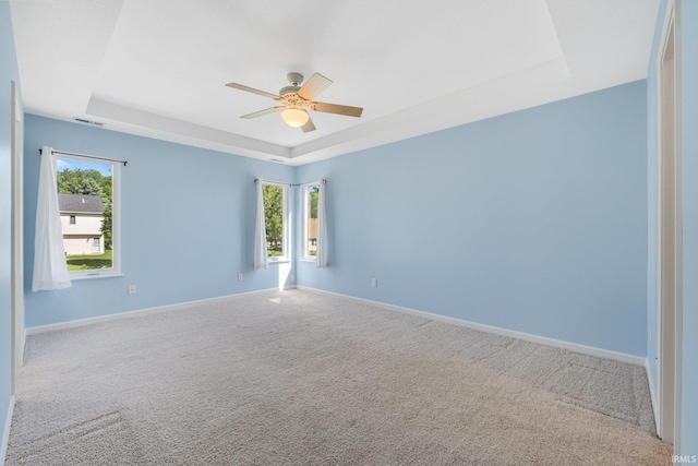 carpeted empty room featuring a raised ceiling, a ceiling fan, and baseboards