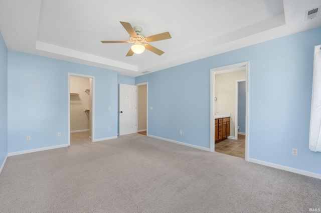 unfurnished bedroom featuring a tray ceiling, light carpet, a walk in closet, and baseboards