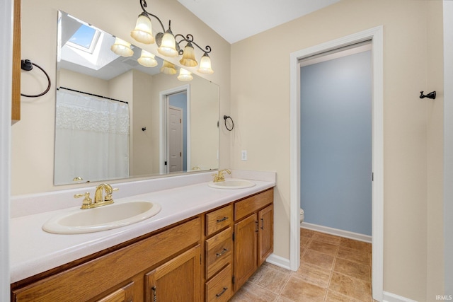 bathroom featuring a skylight, double vanity, toilet, and baseboards