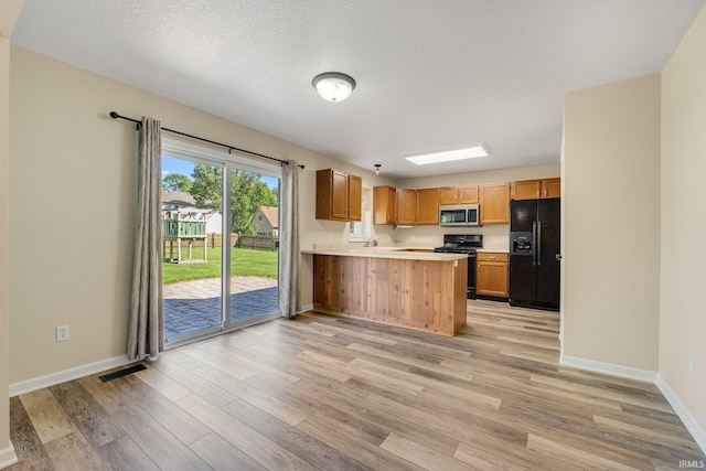 kitchen with black appliances, light countertops, light wood-style floors, a peninsula, and baseboards