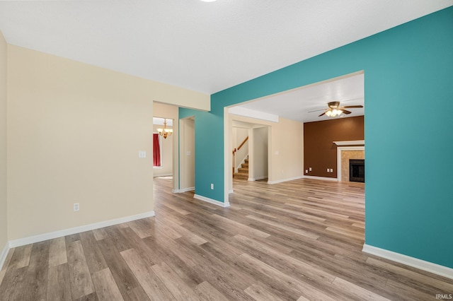 unfurnished living room featuring stairway, a chandelier, wood finished floors, and a fireplace
