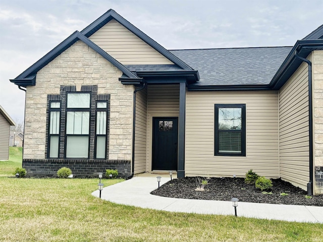 view of front facade with stone siding, a front yard, and roof with shingles