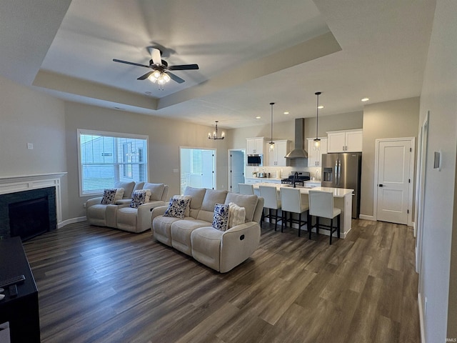 living area featuring a raised ceiling, dark wood-style flooring, a ceiling fan, recessed lighting, and a fireplace