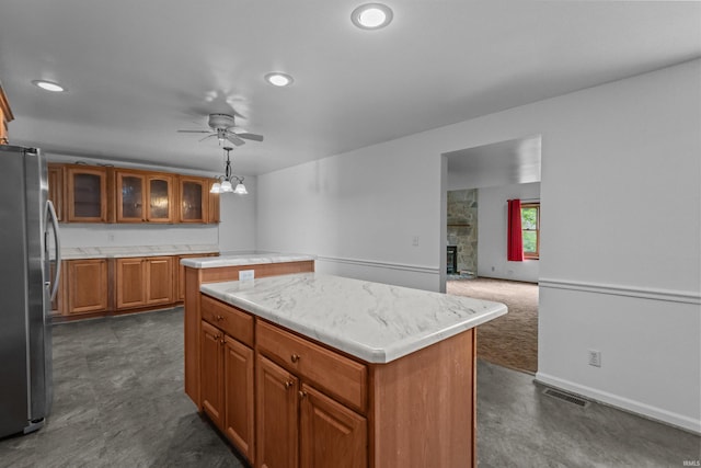 kitchen with freestanding refrigerator, a center island, a ceiling fan, brown cabinets, and light countertops