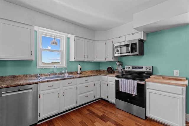 kitchen featuring appliances with stainless steel finishes, a sink, white cabinetry, dark wood-style floors, and dark countertops