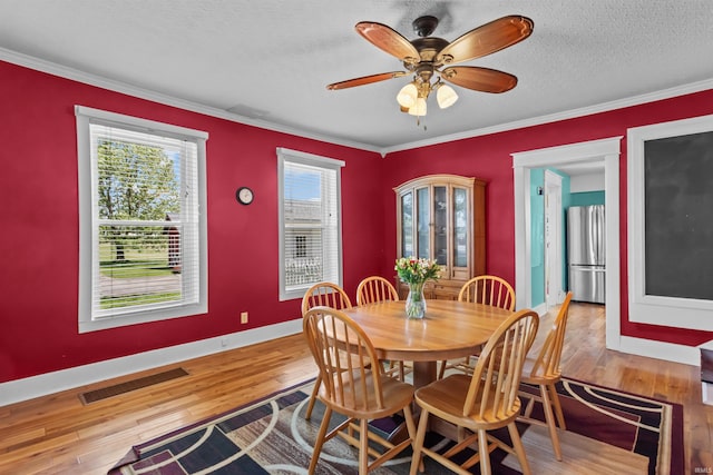 dining space with wood-type flooring, baseboards, crown molding, a ceiling fan, and a textured ceiling