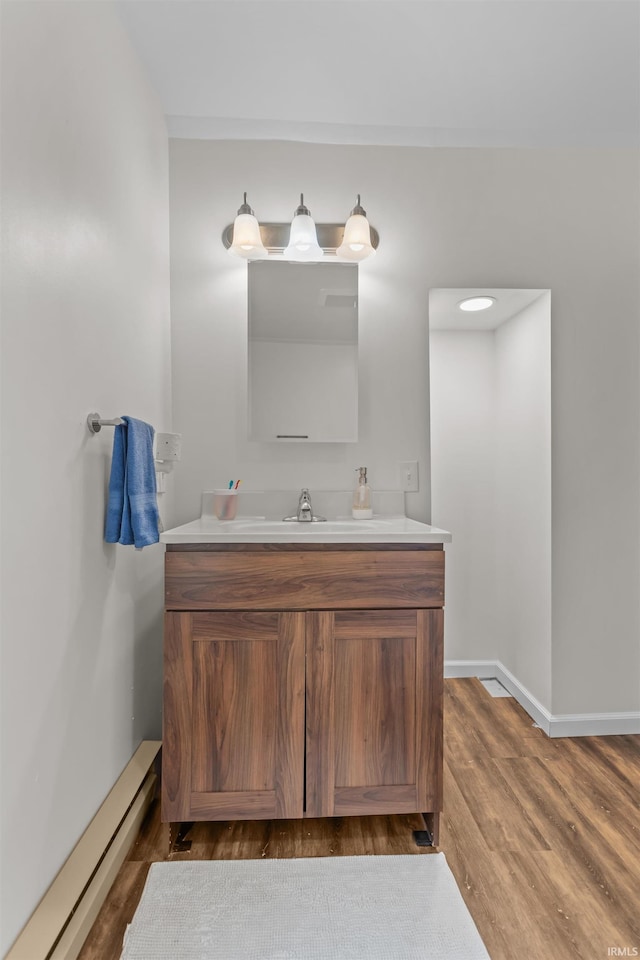 bathroom featuring a baseboard heating unit, vanity, wood finished floors, and baseboards