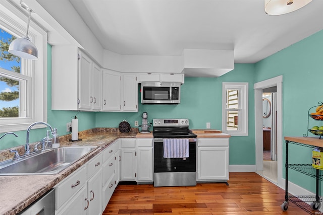kitchen featuring appliances with stainless steel finishes, a sink, white cabinets, light wood-style floors, and pendant lighting
