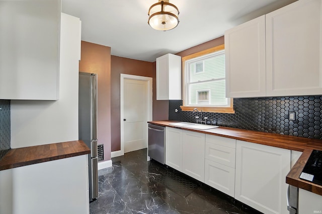 kitchen featuring butcher block countertops, a sink, stainless steel appliances, dark marble finish flooring, and backsplash