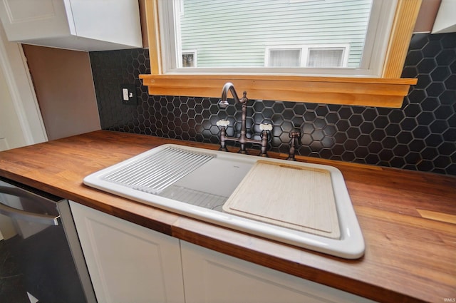 kitchen view of butcher block counters, a sink, white cabinetry, and backsplash