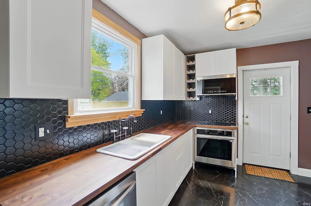 kitchen featuring appliances with stainless steel finishes, a sink, butcher block counters, dark marble finish floors, and white cabinetry